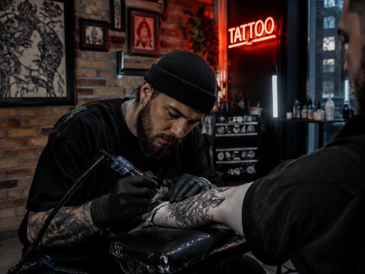 Tatuador fazendo tatuagem no braço de um cliente em estúdio